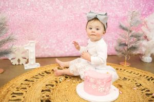 Baby's first birthday cake smash setup with pink backdrop and gold decorations.