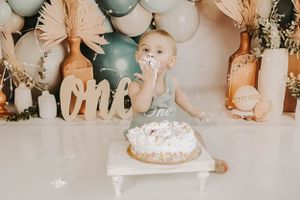A cake smash photoshoot featuring white and sage balloons with decorative pampas grass.