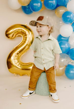 Birthday photoshoot with gold number 2 balloon and blue balloon arch backdrop.