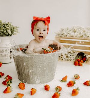 Joyful bath time photo featuring a metal tub surrounded by fresh strawberries and white flowers.