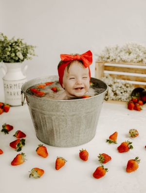 Delightful bath photo with strawberries scattered around a vintage metal tub and floral accents.