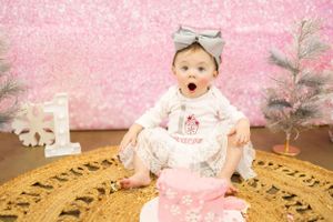 Expressive baby reacting during first birthday cake smash photoshoot with pink backdrop.
