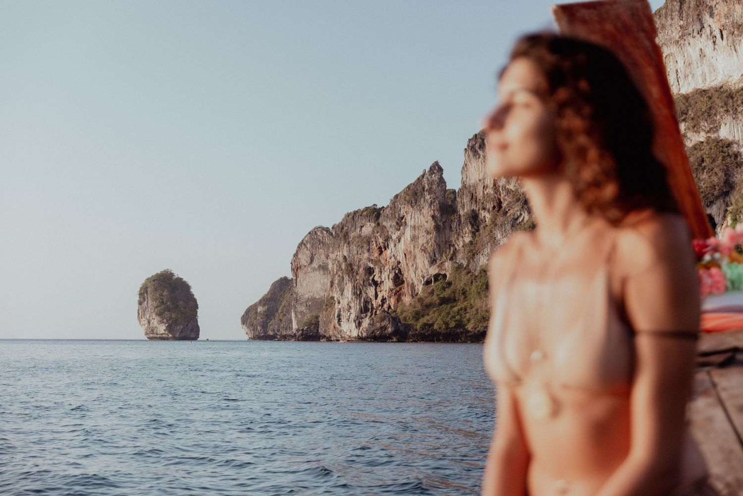Rugged coastal cliffs and rock formations rise from calm ocean waters at sunset.