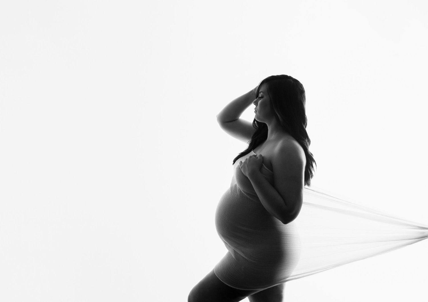 Artistic black and white silhouette maternity photo with dramatic lighting and curves.