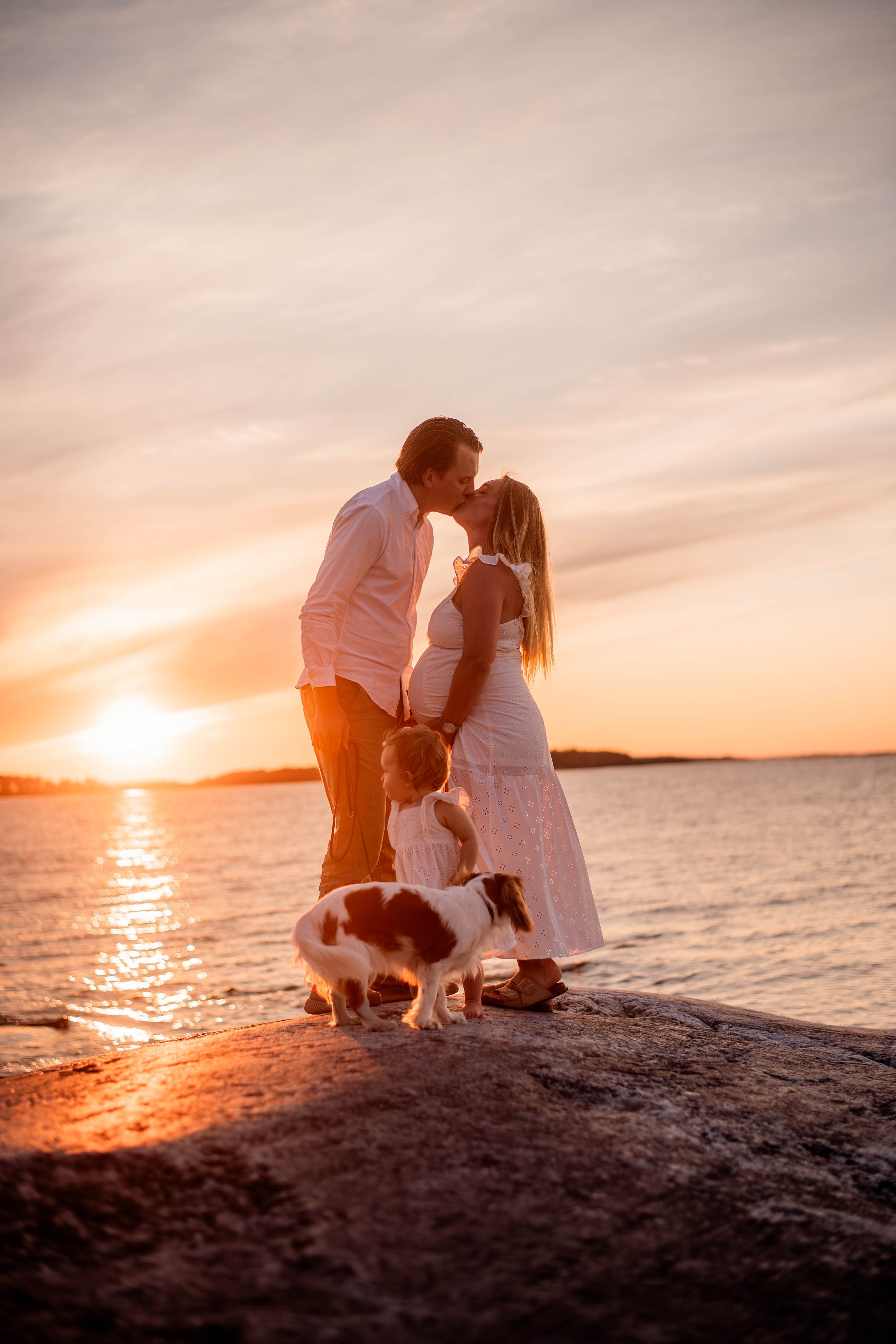 Kärlekspar med deras hund och dotter på en klippa i solnedgången på torö