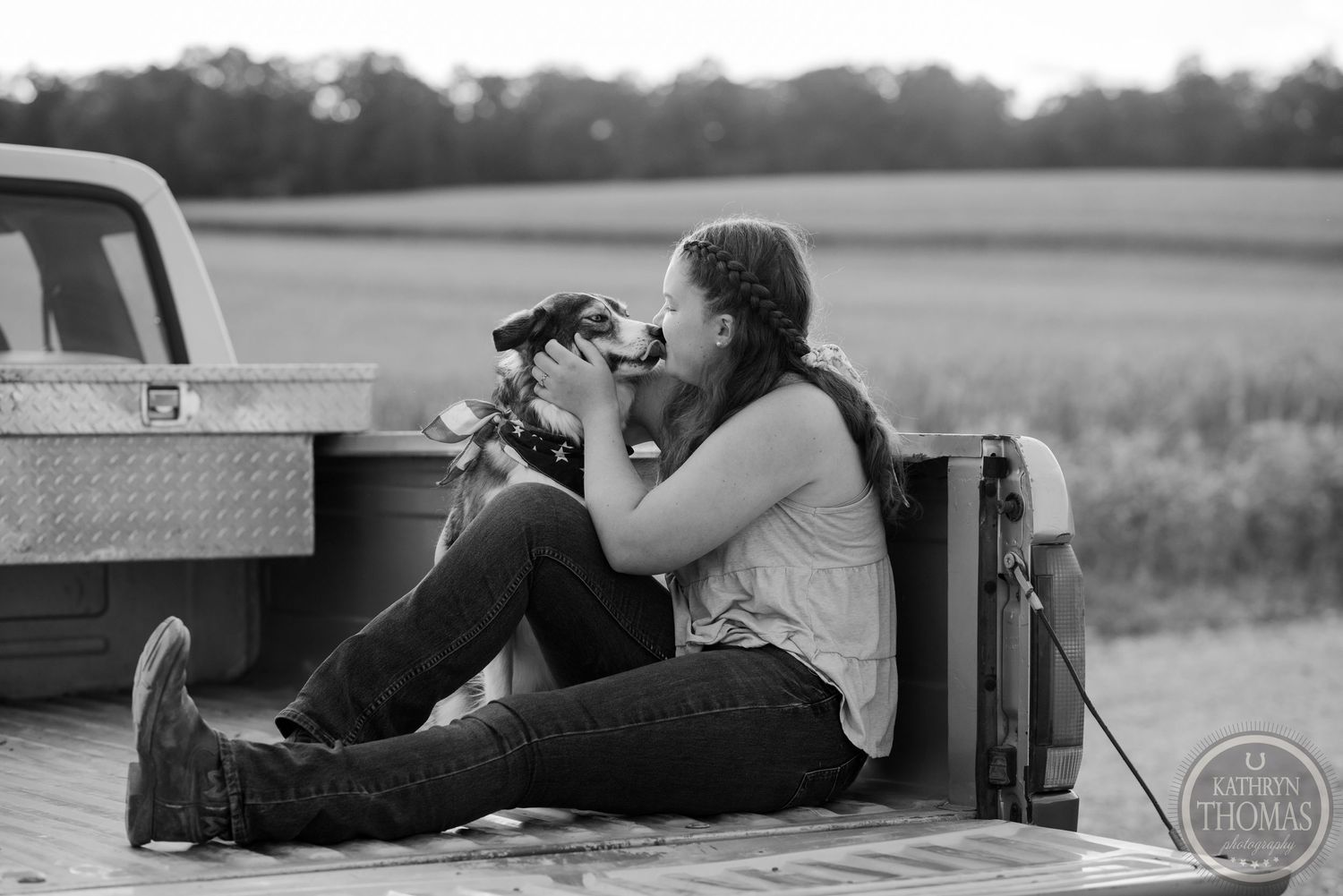 Black and white photo of a photographer sitting on a pickup truck bed taking photos at sunset.