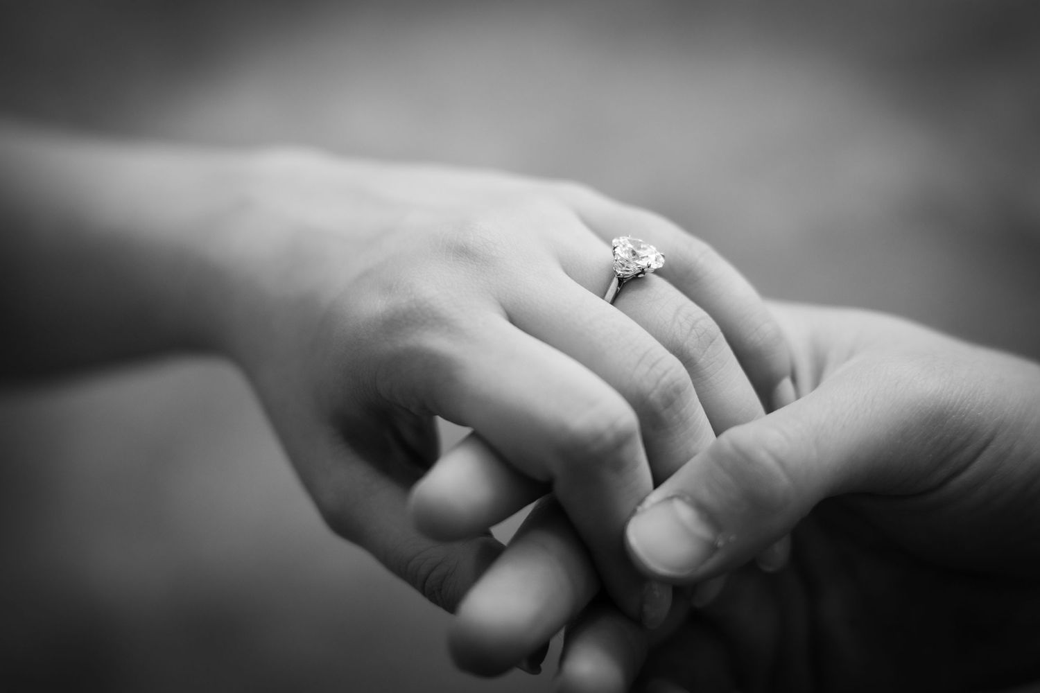 A black and white close-up of hands displaying an engagement ring.