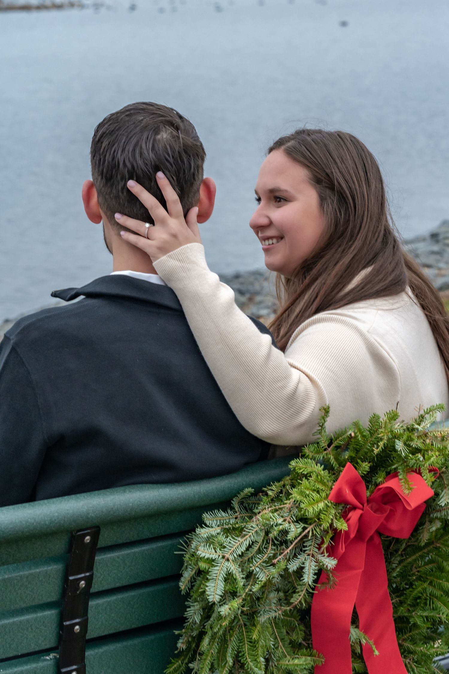 A couple shares an intimate moment on a bench with a holiday wreath beside them.