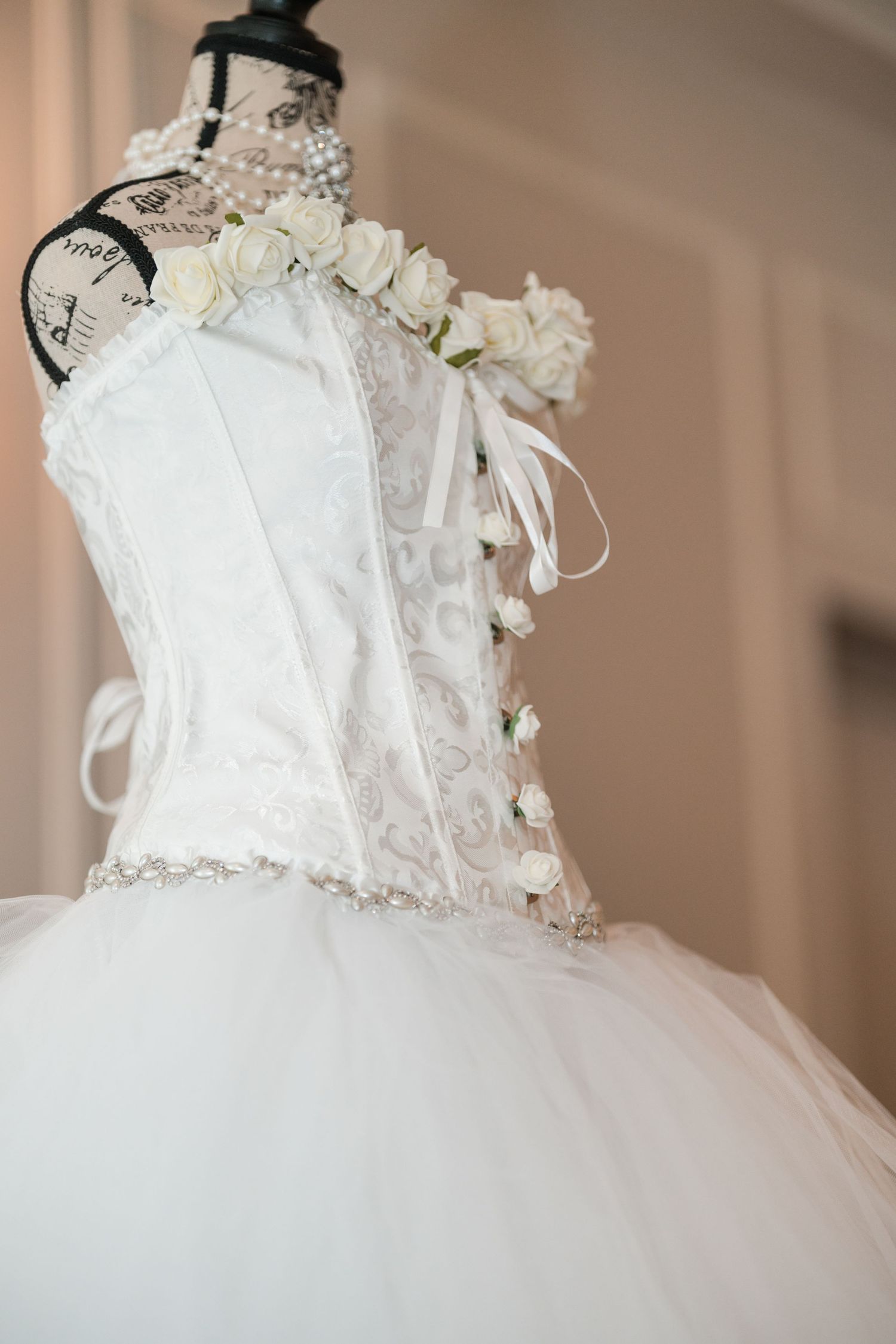 A white wedding dress bodice with lace details and floral embellishments on a mannequin.