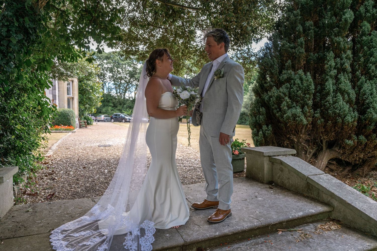A bride and groom share an intimate moment on stone steps surrounded by greenery.