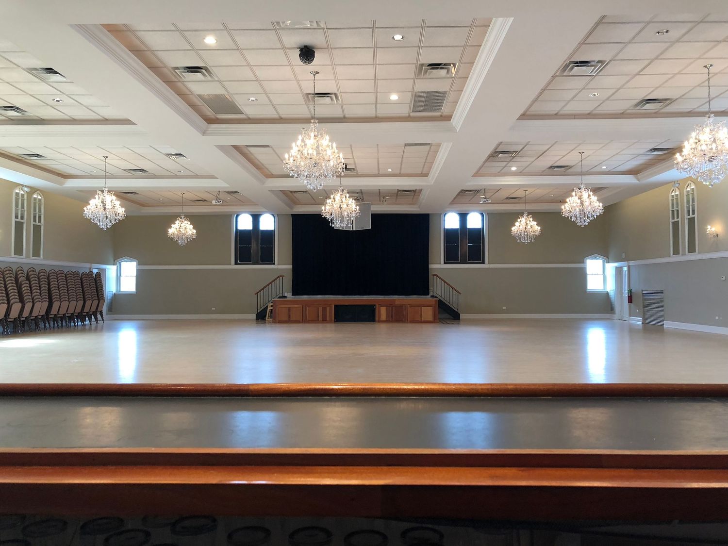 Event venue with raised stage, multiple crystal chandeliers and tiered ceiling design.