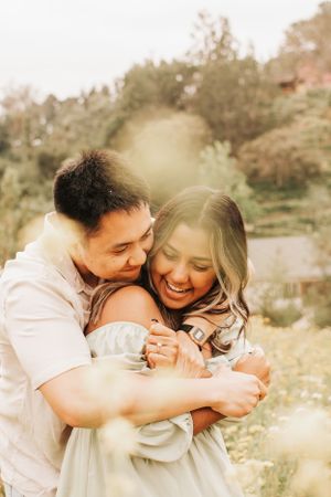 Candid shot of a couple sharing a warm embrace and genuine laughter in nature.