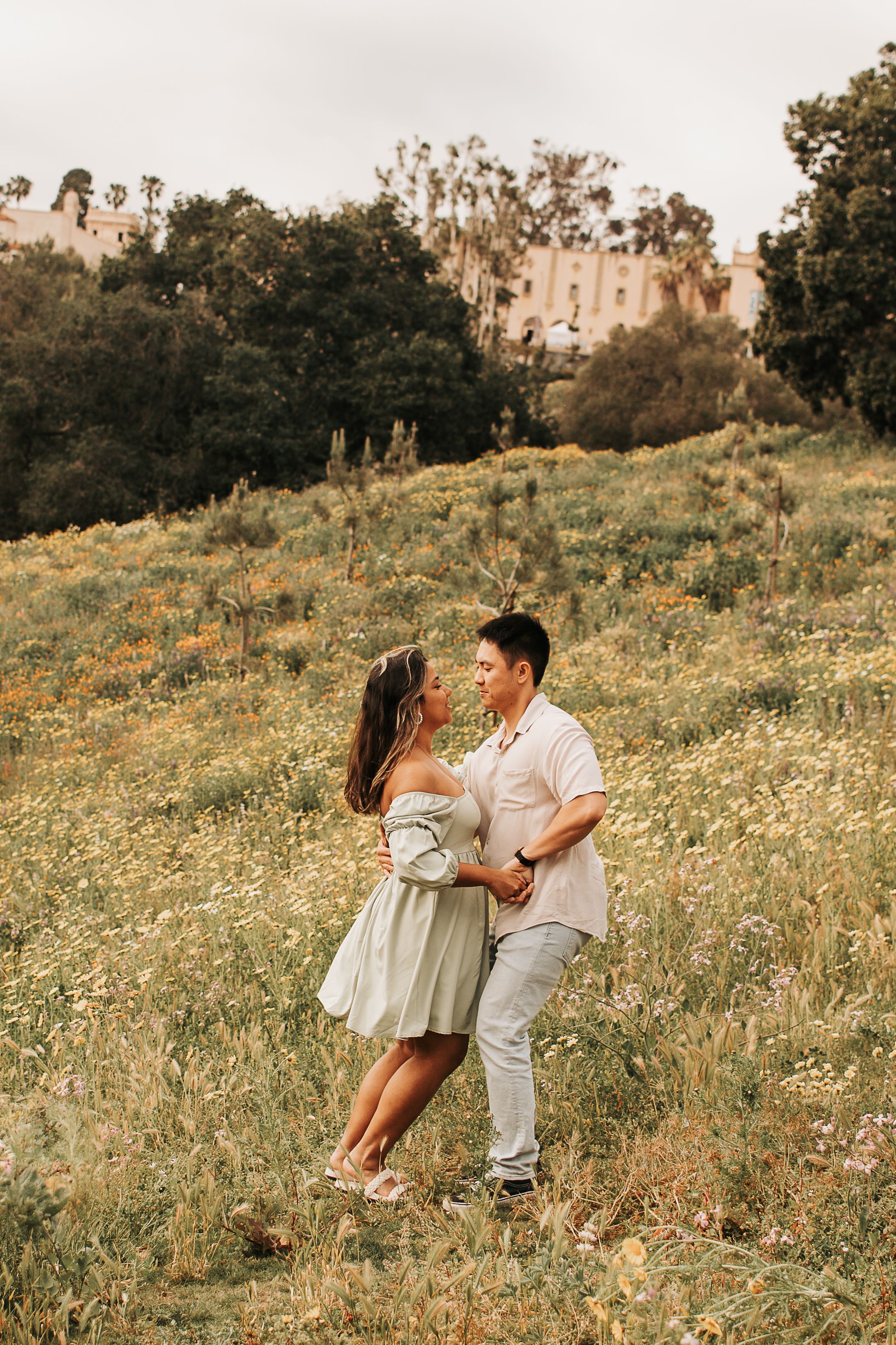 Couple in light summer clothing embracing on hillside covered in wildflowers.