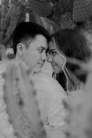 Intimate black and white portrait of a couple gazing at each other through greenery.
