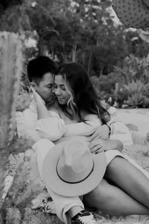 Black and white photo of couple sharing tender moment outdoors with hat and desert plants.