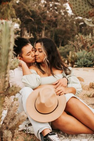 Affectionate moment between couple in white outfits sitting among cacti.