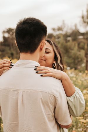 A close embrace captured from behind shows a couple's tender moment in a flower field.