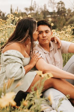 A couple gets cozy in a meadow filled with golden flowers during a warm afternoon photoshoot.