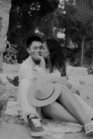 Intimate black and white portrait of couple sitting together with hat in desert setting.