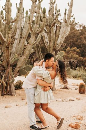 A romantic moment between a couple among desert cacti and sandy terrain.