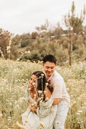 A joyful couple laughs together in a sunny field of white wildflowers.