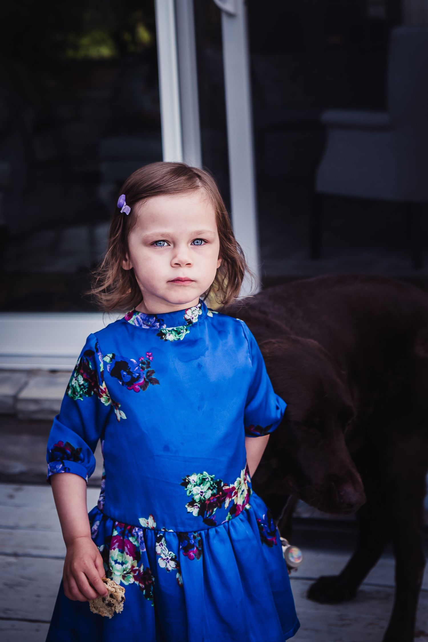 A young girl in a blue silk dress with embroidered flowers looks at the camera.