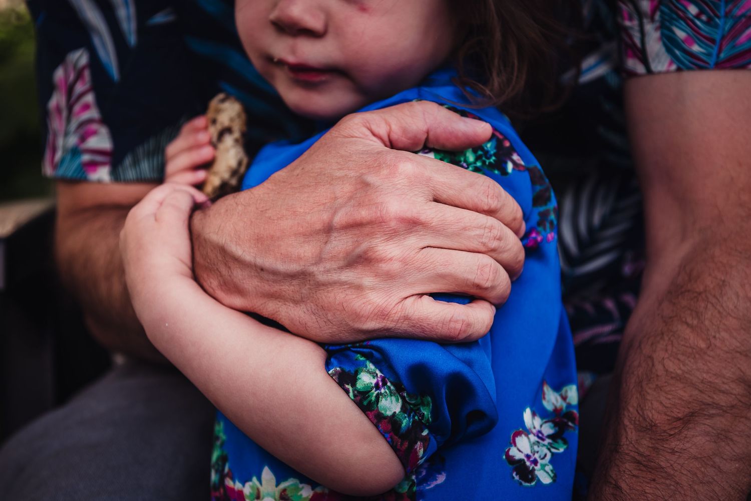 Close up colour image of a father's hand holding his daughter as she holds his arm.