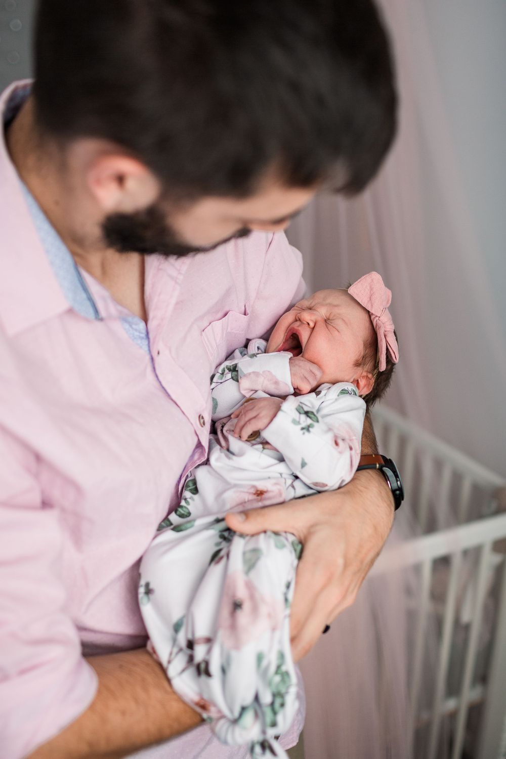 A tender moment between parent and newborn baby wrapped in floral swaddle.