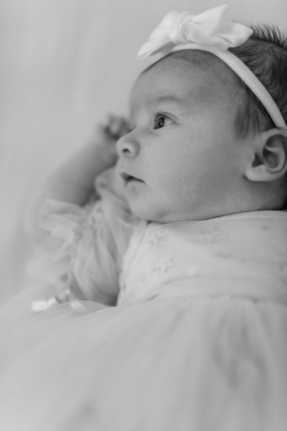 Close-up black and white portraits of a sleeping newborn baby wearing a white bow.