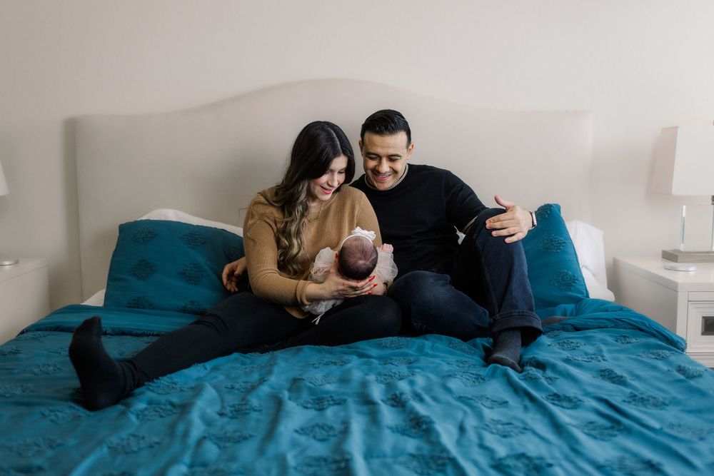 New parents sitting on blue bed sharing intimate moment with their newborn baby.