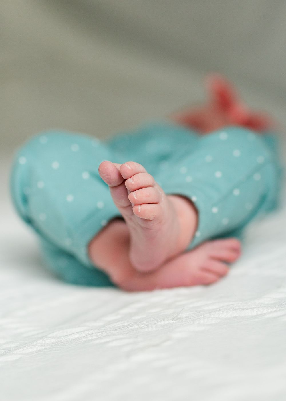 Tiny baby feet in polka dot mint green clothing against white fabric, by best San Antonio Photographer.