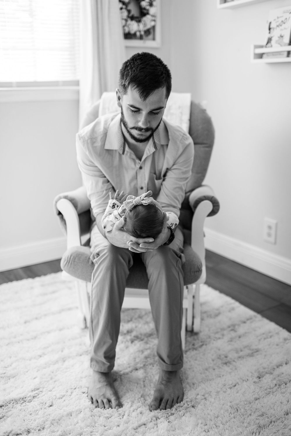 A black and white portrait of a parent holding a newborn while sitting in a nursery chair, by best San Antonio Photographer.