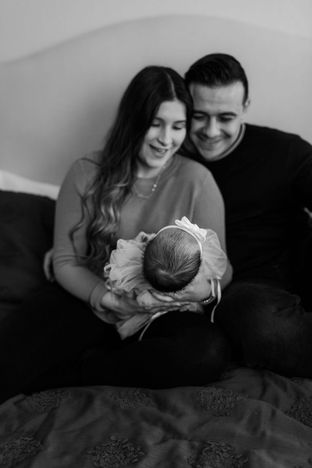 Black and white portrait of new parents on couch cradling their sleeping newborn.