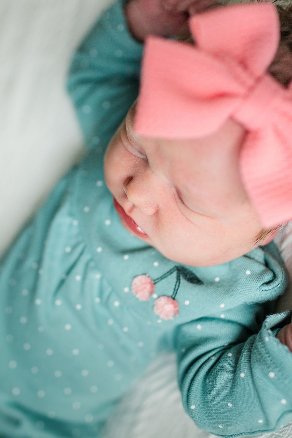 A sleeping baby wearing a mint green outfit and pink bow in soft lighting, by best San Antonio Photographer.