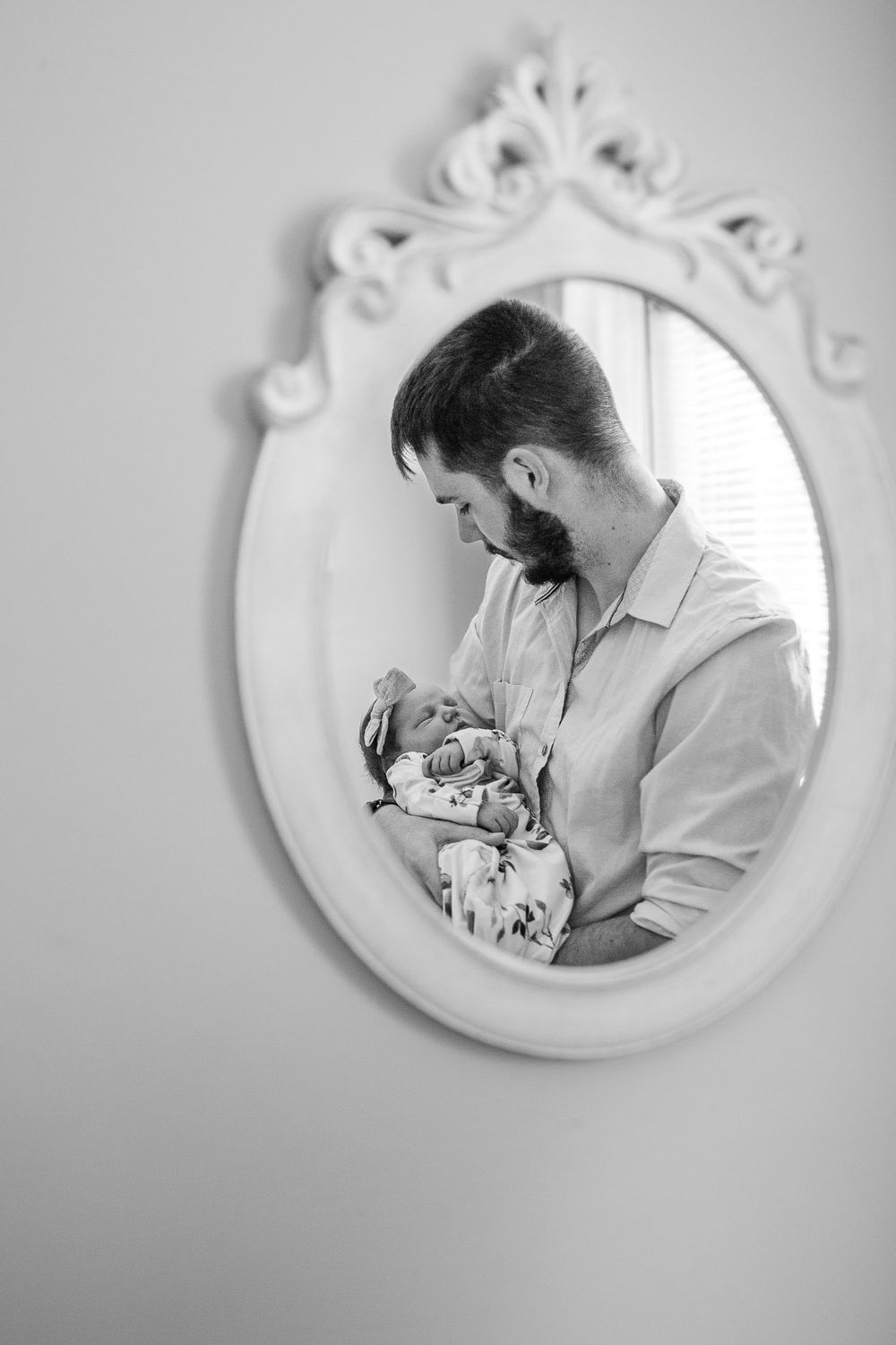 Black and white reflection in ornate mirror of tender moment between father and newborn baby.