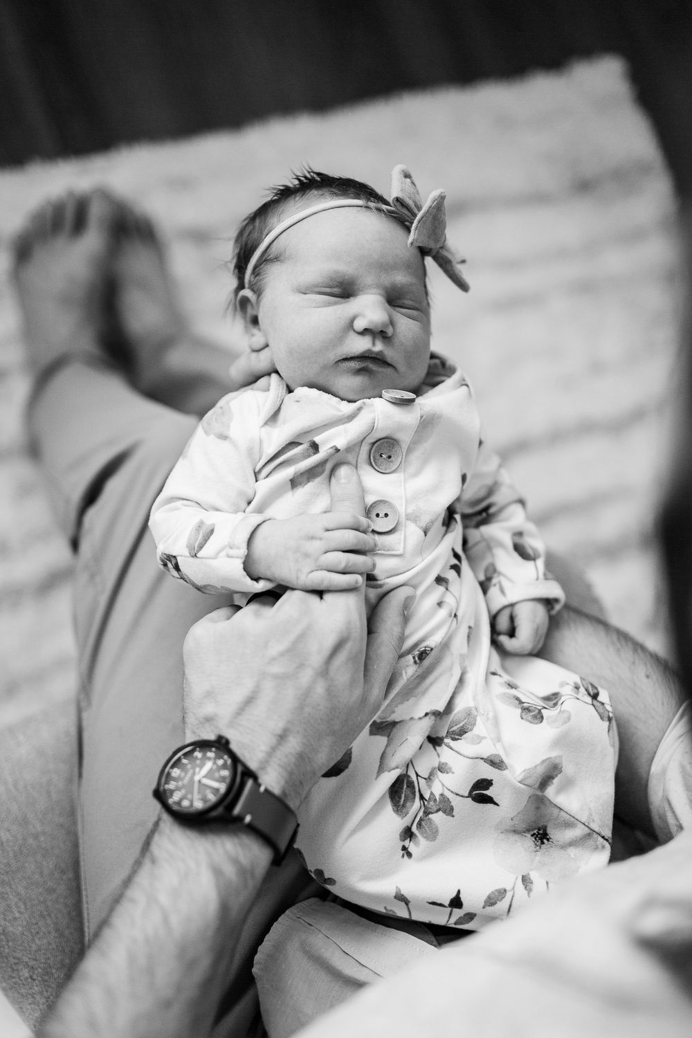 Black and white photo of sleeping newborn wearing bow headband and floral outfit.