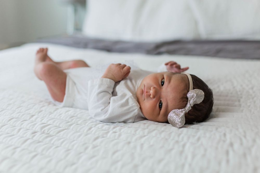 Newborn baby in white clothing resting peacefully on white bedding.