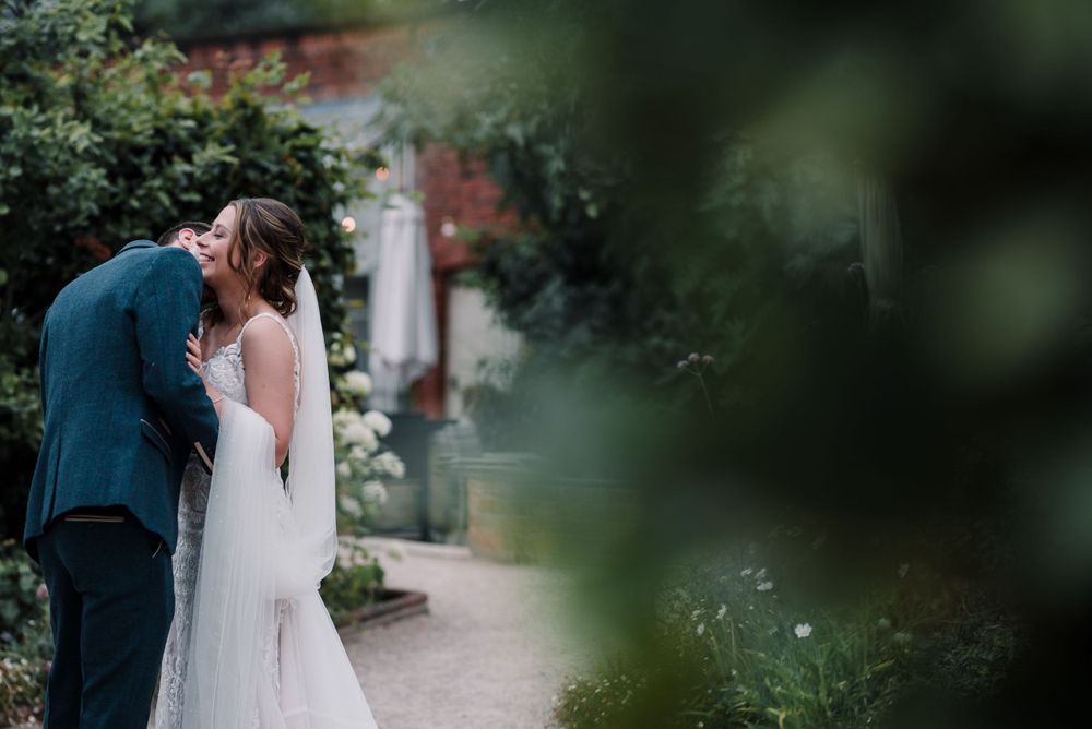 A couple shares an intimate moment in a lush garden setting during their wedding day.