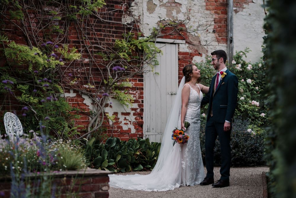 Garden wedding scene with rustic brick wall and flowering plants in background.