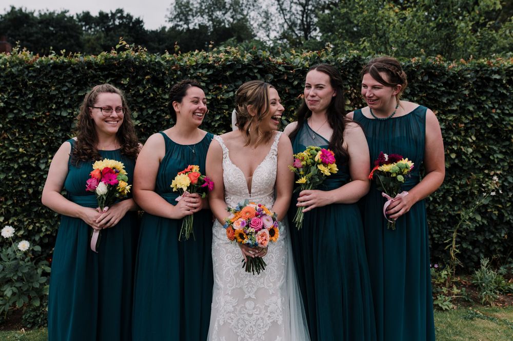 Wedding party in dark teal dresses holding colorful bouquets against garden backdrop.