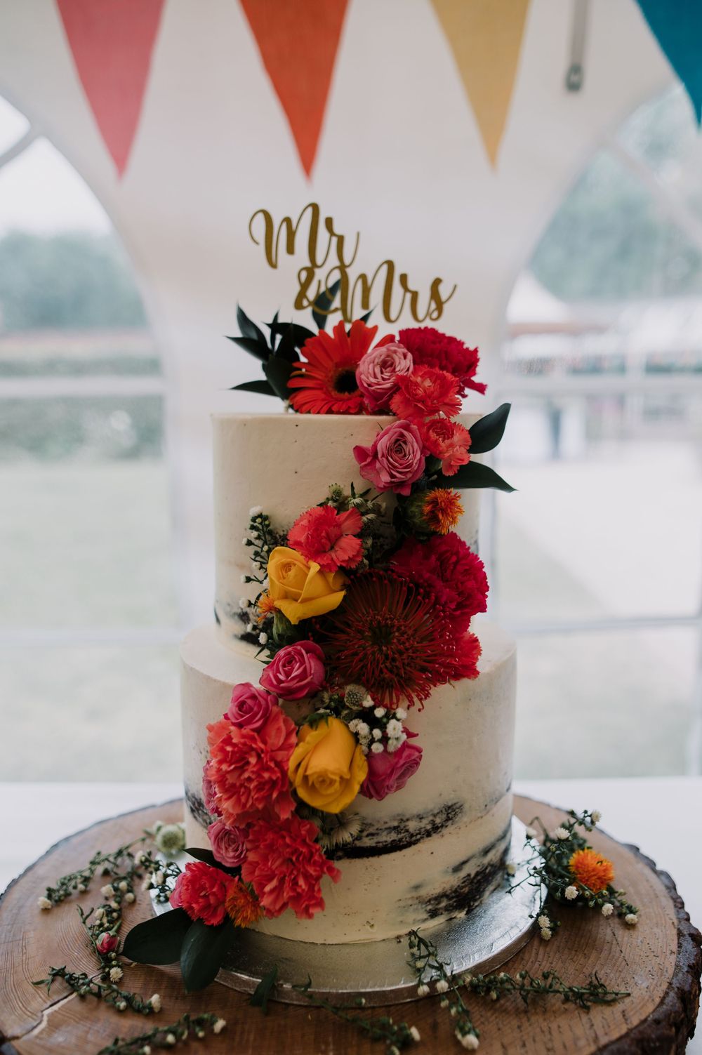 Three-tier wedding cake decorated with cascading red and yellow flowers and Mr & Mrs topper.