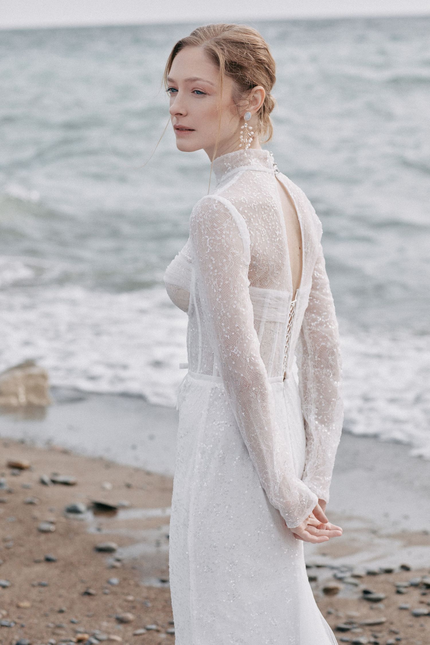 Elegant bridal gown with high neck and sheer lace details photographed by the ocean.
