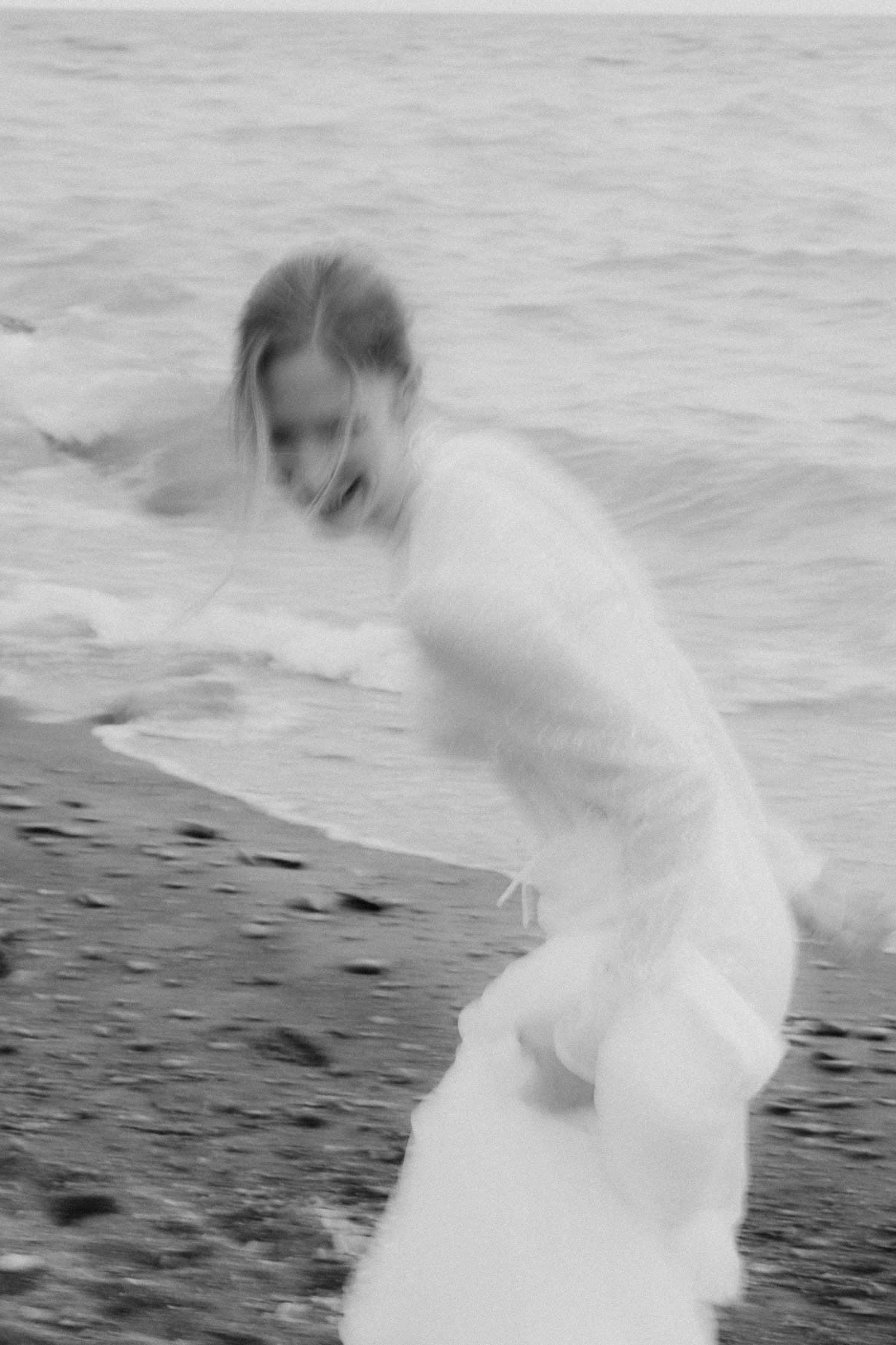 Artistic motion blur photograph of white wedding dress on beach in black and white.