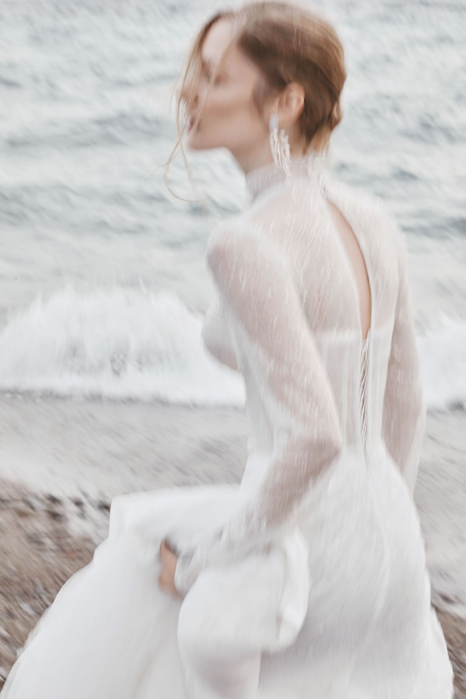 Dreamy beach bridal portrait featuring a flowing white gown with delicate lace sleeves in soft focus.