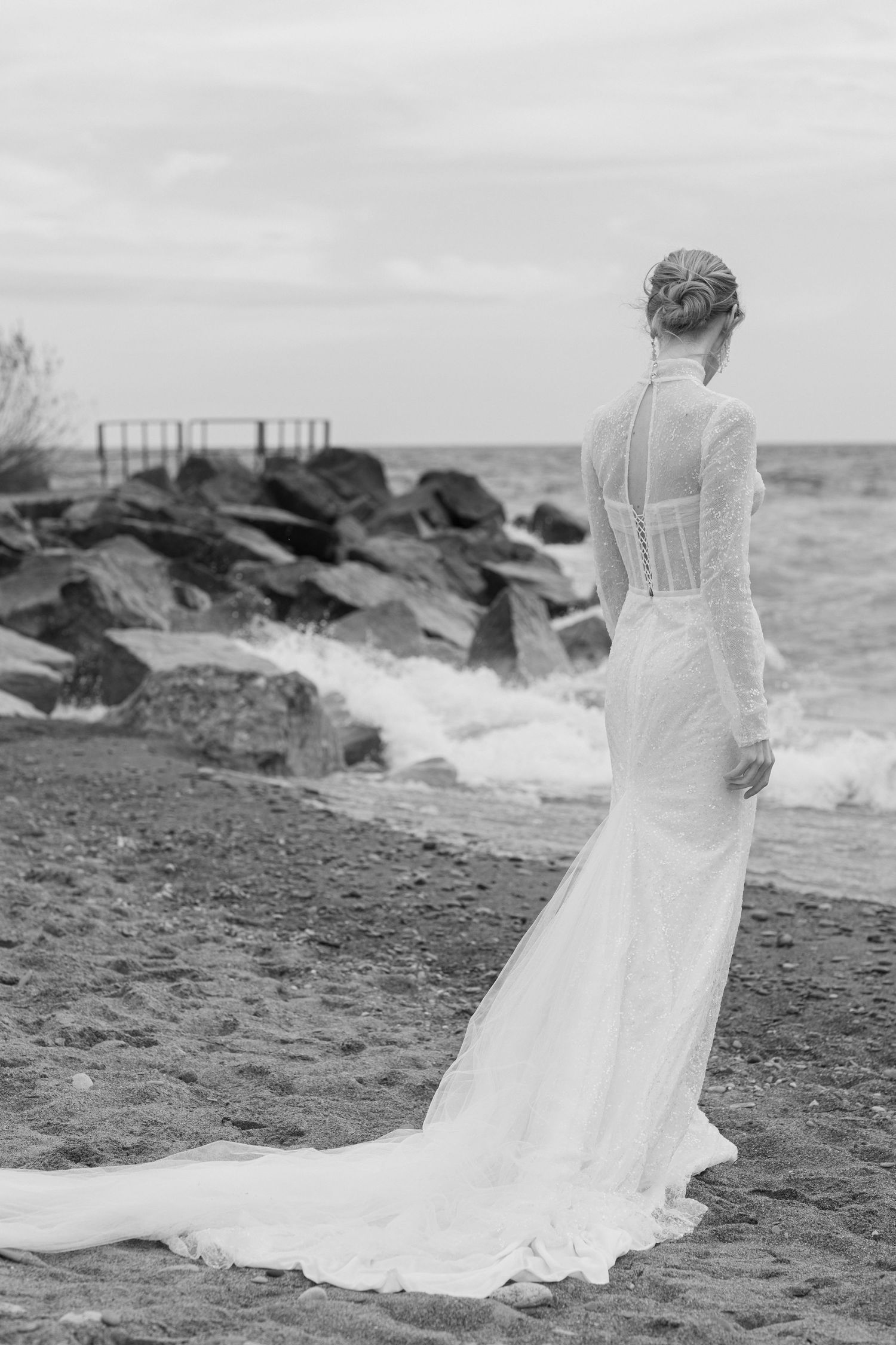 Black and white photo of wedding dress with dramatic train on rocky beach shoreline.