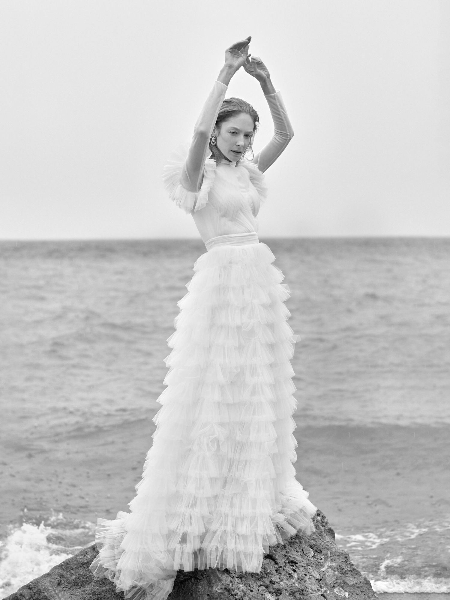 Dramatic bridal portrait on rocky coastline featuring tiered tulle wedding gown.