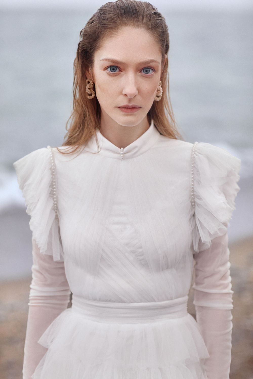 Victorian-inspired white wedding dress with high neck and structured shoulders against seaside backdrop.