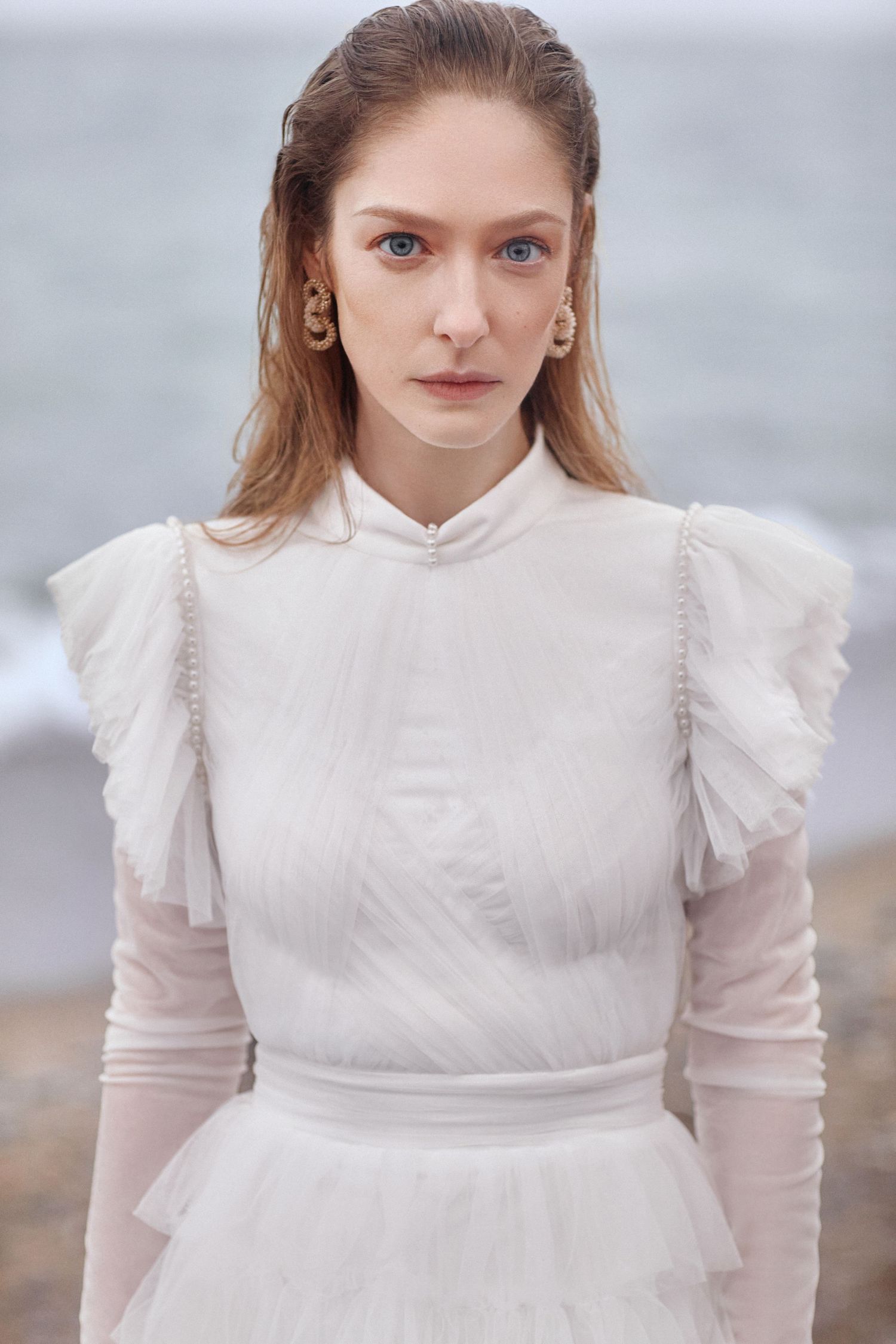 Victorian-inspired white wedding dress with high neck and structured shoulders against seaside backdrop.