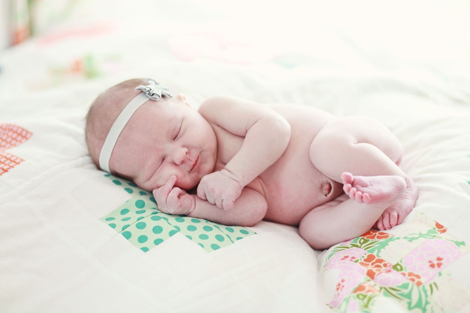 Sleeping newborn baby wearing headband on floral patterned blanket.