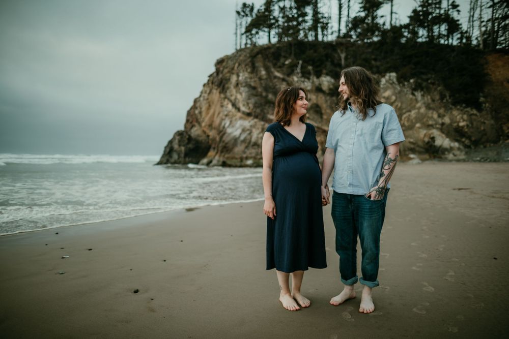 couple holds hands while looking at each other on the coast maternity photographer portland oregon